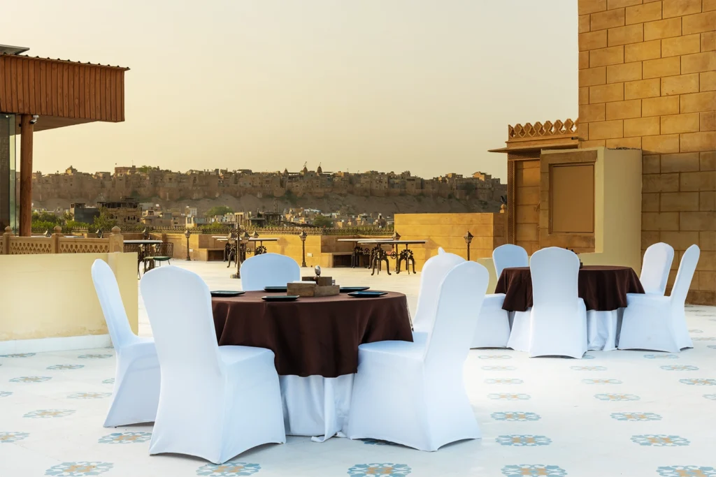 a table set up with white chairs and a brown tablecloth